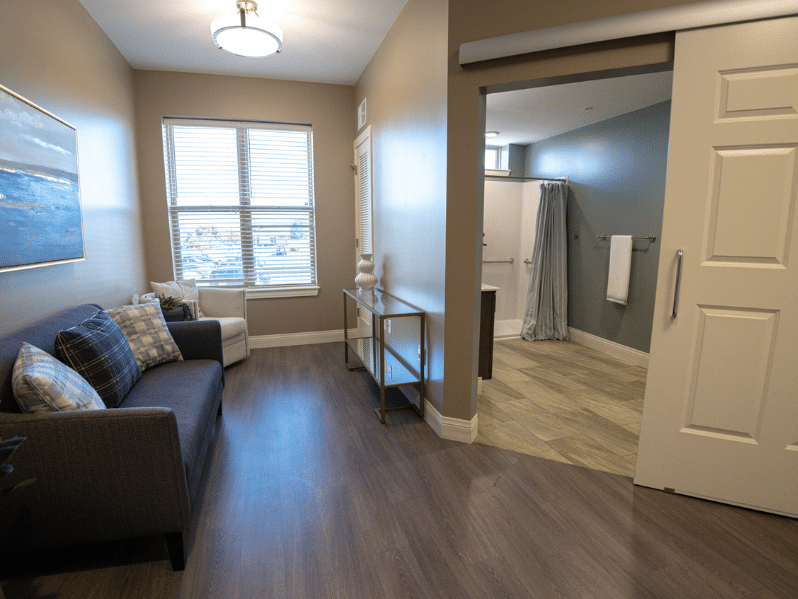 Memory Support apartment area showing a couch in front of a window and the restroom doorway