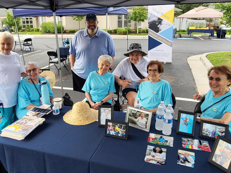 Group of volunteers posing for picture around a table at an outdoors event