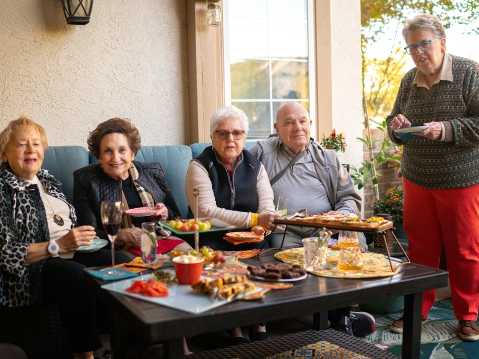 Five residents sitting around a patio table that is topped with Hors d'oeuvres