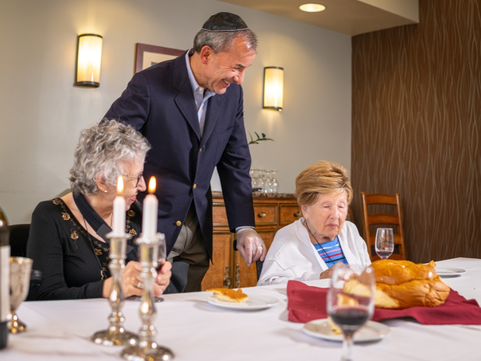 Simon Abrahms smiling with two residents and a dining table