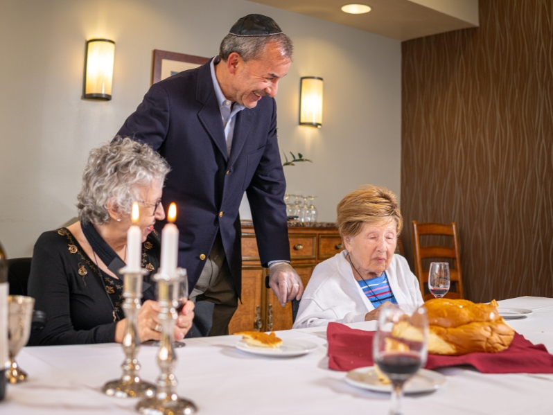 Simon Abrahms smiling with two residents and a dining table