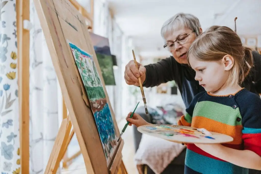 An elderly woman painting with her granddaughter from her home at Village Shalom, offering senior living in Overland Park in KS.