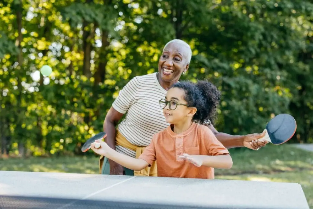 A senior woman with her granddaughter playing ping pong as a part of intergenerational activities at Village Shalom, offering senior living in Overland Park, KS.