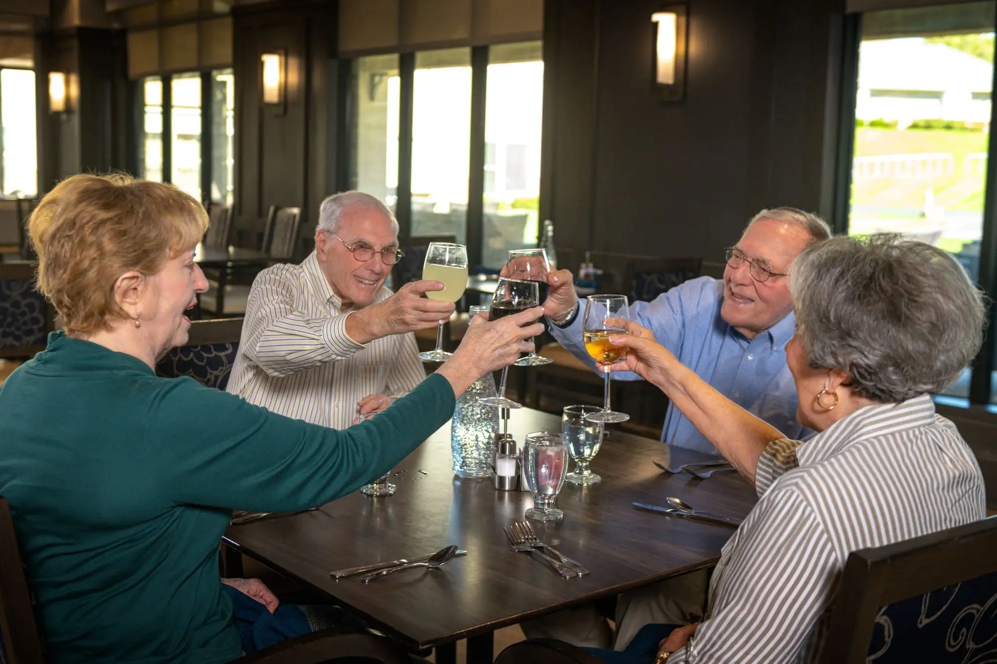 4 older adults toasting while having wine from their home at Village Shalom, a Jewish Senior Living Community in Overland Park, KS.