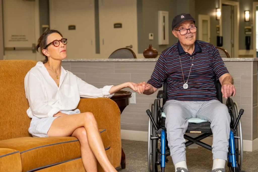 Image of an adult daughter holding her senior fathers hand while learning about the memory care difference at Village Shalom in Overland Park, KS.