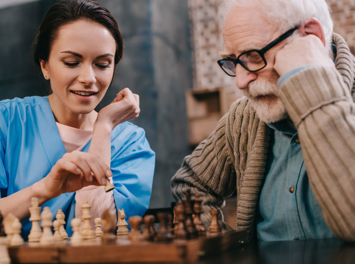 A senior man and a health care staff play chess together in a Kansas City Alzheimers care facility