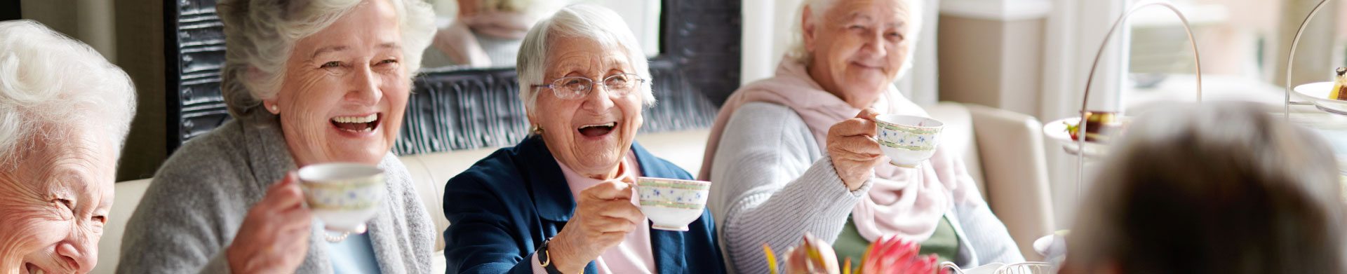 Elderly women hold up fine china tea cups and smile for the camera