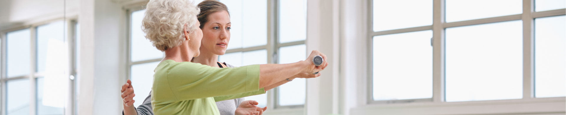 A physical therapist helps a senior woman exercise with weights